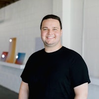 a man in a black shirt standing in front of a white wall